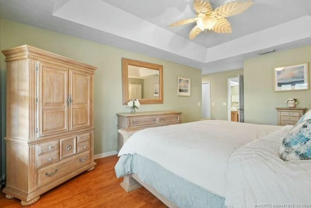 bedroom with ceiling fan, ensuite bathroom, a tray ceiling, a closet, and light wood-type flooring