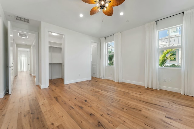 unfurnished bedroom featuring light wood-type flooring, a walk in closet, and ceiling fan