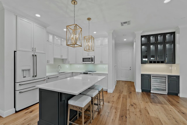 kitchen featuring appliances with stainless steel finishes, light wood-type flooring, white cabinets, a center island, and wine cooler