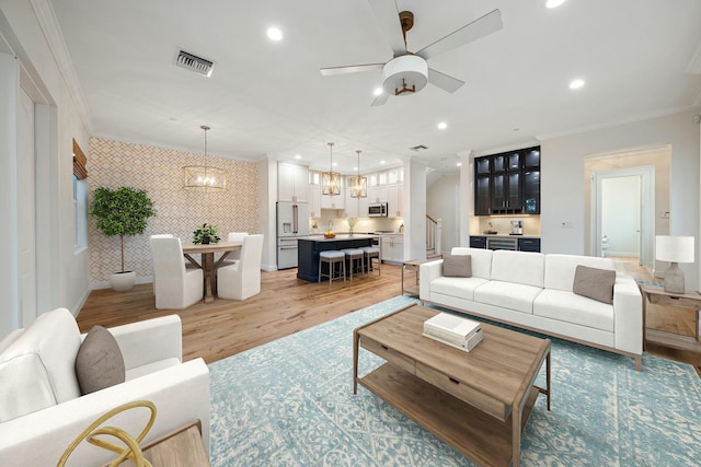 living room with ceiling fan with notable chandelier, light hardwood / wood-style floors, ornamental molding, and sink