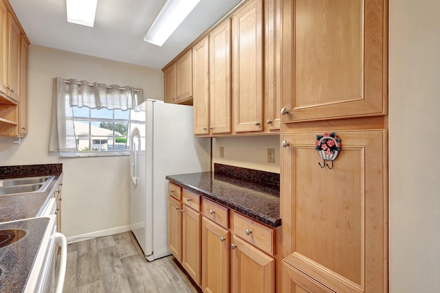 kitchen with sink, white refrigerator, dark stone countertops, light brown cabinetry, and light wood-type flooring