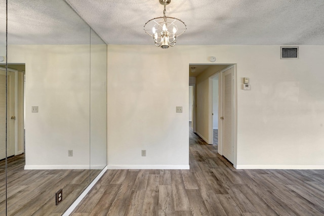 empty room featuring a chandelier, wood-type flooring, and a textured ceiling