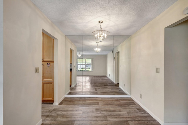 corridor with wood-type flooring, a textured ceiling, and a notable chandelier