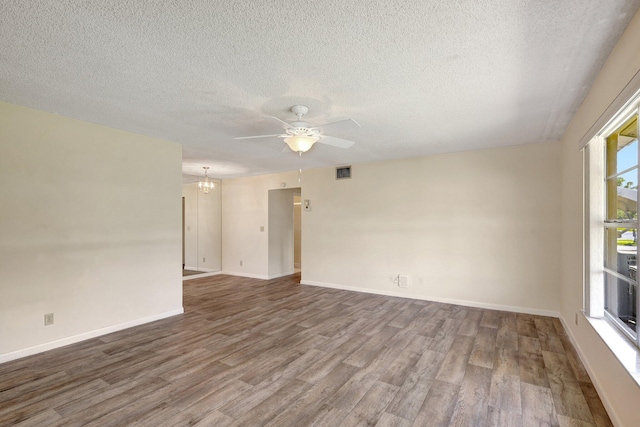 empty room featuring hardwood / wood-style flooring, ceiling fan with notable chandelier, a healthy amount of sunlight, and a textured ceiling