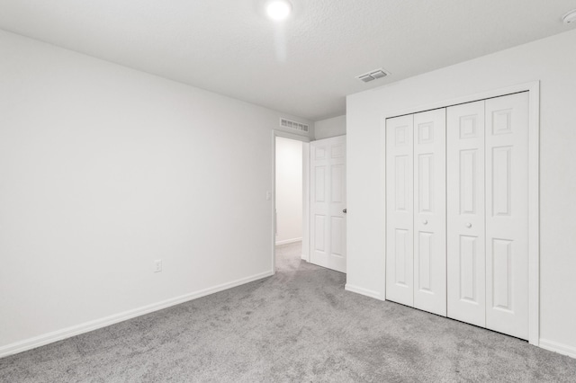 unfurnished bedroom featuring a textured ceiling, light colored carpet, and a closet