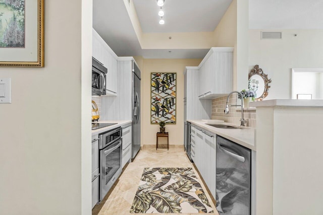 kitchen featuring backsplash, stainless steel appliances, a tray ceiling, sink, and white cabinetry