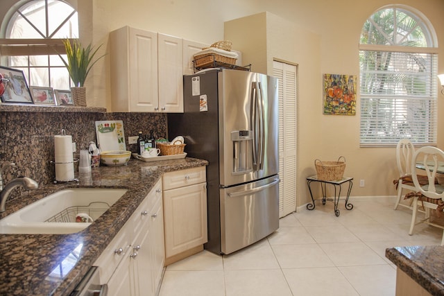 kitchen featuring sink, stainless steel fridge, dark stone counters, decorative backsplash, and light tile patterned floors