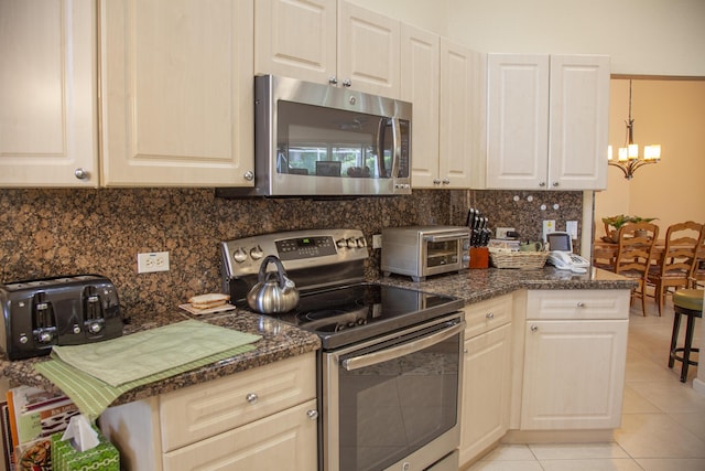 kitchen featuring dark stone counters, an inviting chandelier, light tile patterned floors, tasteful backsplash, and stainless steel appliances