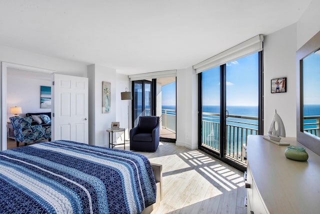 bedroom with access to exterior, a water view, light hardwood / wood-style flooring, and multiple windows