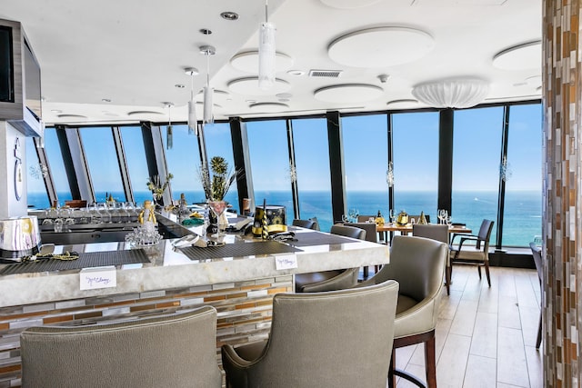 kitchen featuring light hardwood / wood-style floors, a water view, hanging light fixtures, and a wall of windows