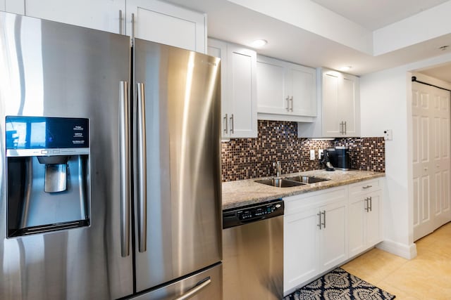 kitchen featuring light stone countertops, appliances with stainless steel finishes, backsplash, light tile patterned floors, and white cabinets