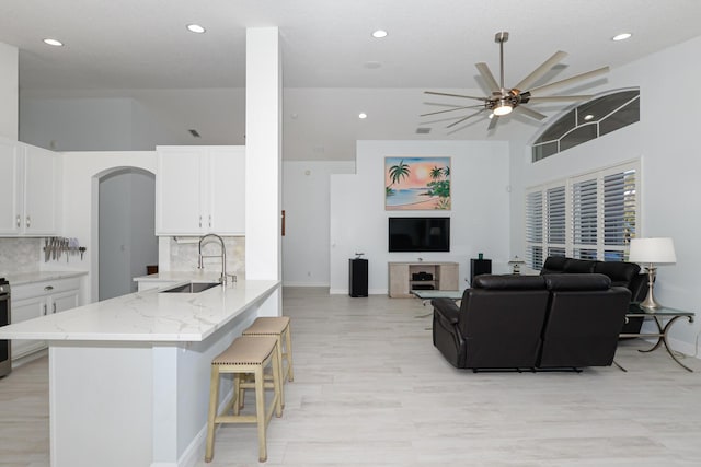 kitchen featuring light stone countertops, backsplash, sink, white cabinets, and a breakfast bar area