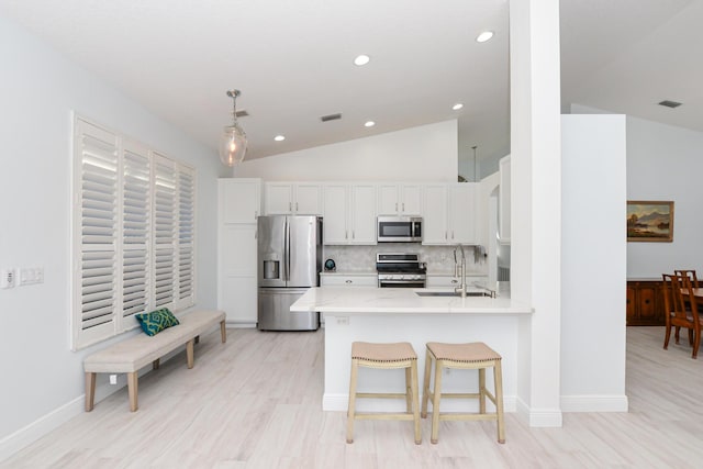 kitchen with decorative backsplash, appliances with stainless steel finishes, kitchen peninsula, white cabinetry, and lofted ceiling