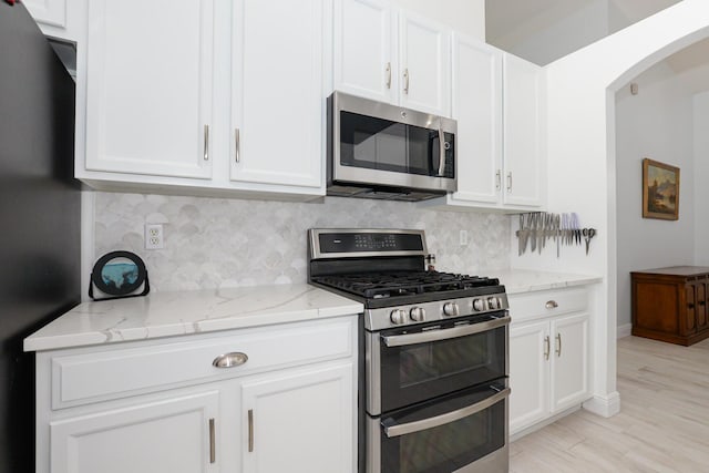 kitchen with light stone countertops, white cabinetry, tasteful backsplash, light hardwood / wood-style floors, and appliances with stainless steel finishes