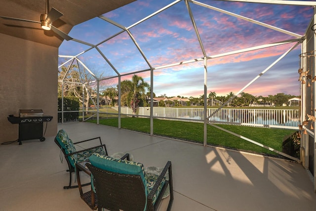 patio terrace at dusk with a yard, a water view, area for grilling, and glass enclosure