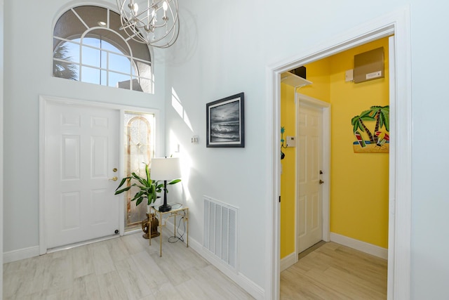 foyer entrance featuring light hardwood / wood-style flooring, a towering ceiling, and a notable chandelier