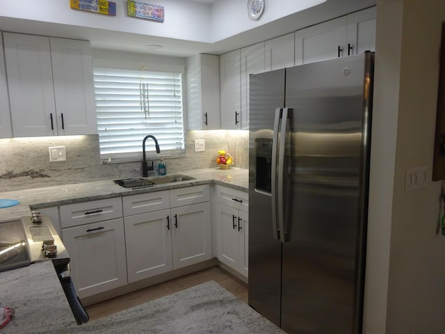 kitchen featuring light stone countertops, stainless steel fridge, tasteful backsplash, sink, and white cabinets