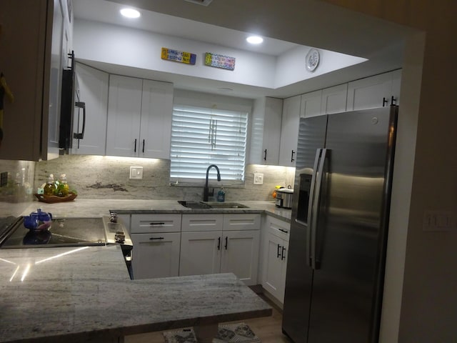 kitchen featuring white cabinetry, sink, light stone countertops, backsplash, and stainless steel fridge