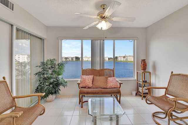 sitting room featuring ceiling fan, a water view, light tile patterned flooring, and a textured ceiling