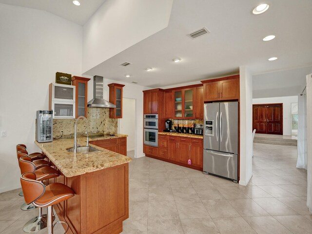 kitchen featuring backsplash, kitchen peninsula, wall chimney exhaust hood, and appliances with stainless steel finishes