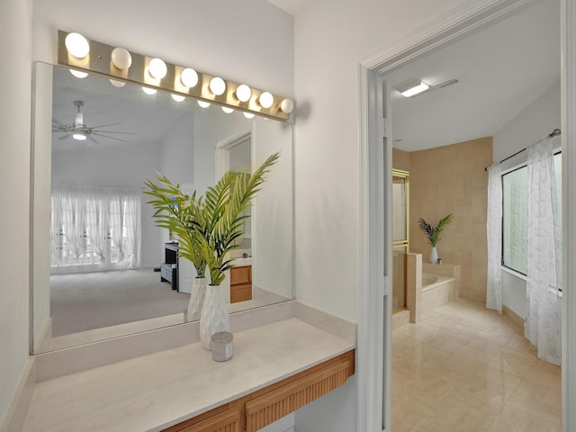 bathroom with tiled bath, ceiling fan, vanity, and a healthy amount of sunlight