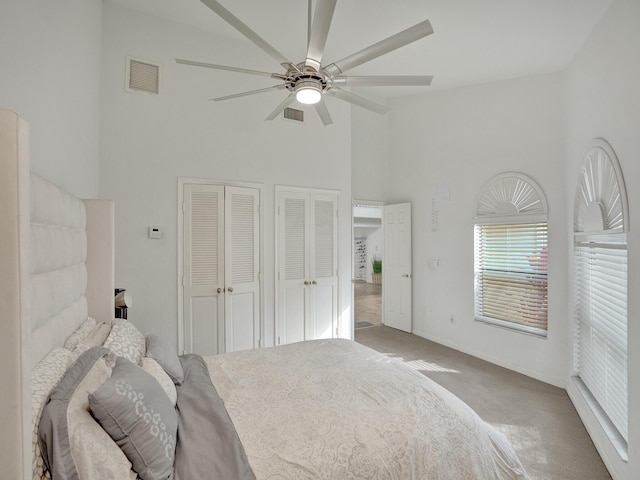 bedroom with a high ceiling, light colored carpet, ceiling fan, and multiple closets