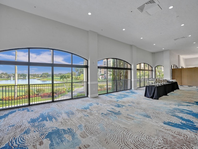 interior space featuring a towering ceiling, a textured ceiling, access to outside, light colored carpet, and a water view