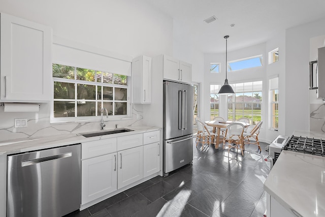 kitchen featuring pendant lighting, sink, decorative backsplash, white cabinetry, and stainless steel appliances