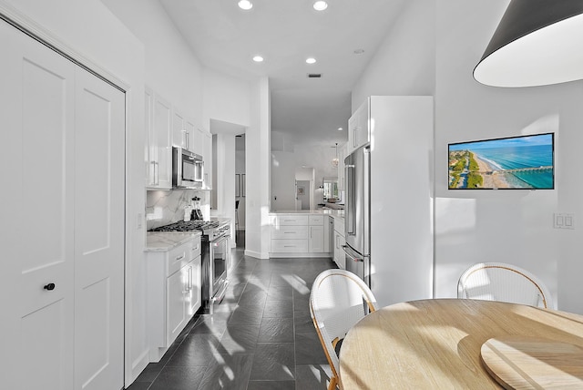 kitchen with white cabinets, premium appliances, light stone counters, and a towering ceiling