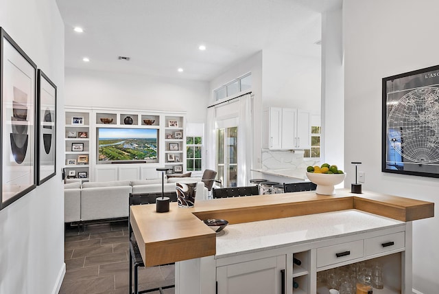 kitchen with light stone countertops, a center island, a breakfast bar area, decorative backsplash, and white cabinets