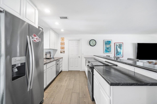 kitchen with stainless steel appliances, dark countertops, visible vents, white cabinets, and light wood-type flooring