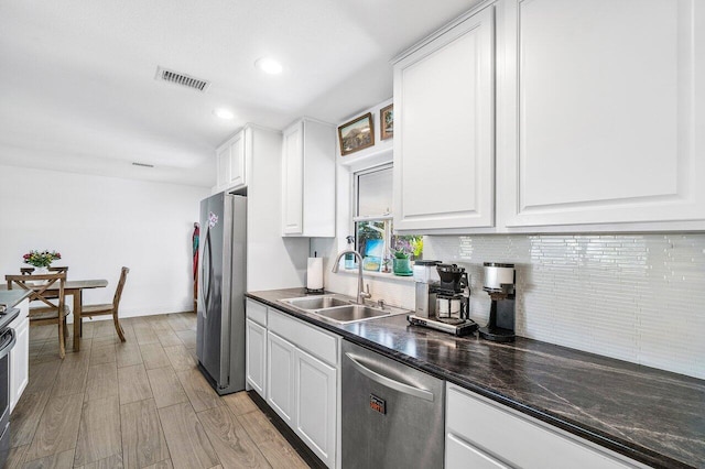 kitchen featuring visible vents, white cabinets, dark countertops, stainless steel appliances, and a sink