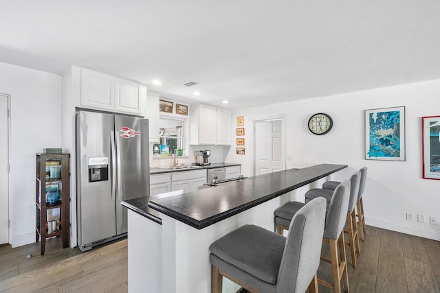 kitchen with a breakfast bar area, dark countertops, white cabinetry, a sink, and stainless steel fridge