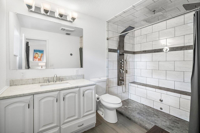 bathroom featuring visible vents, vanity, a tile shower, and toilet