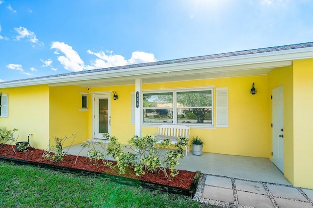 doorway to property with covered porch, roof with shingles, and stucco siding