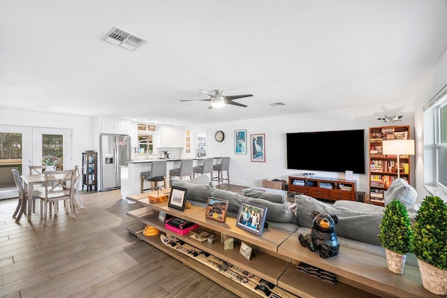 living area with a ceiling fan, french doors, visible vents, and light wood finished floors