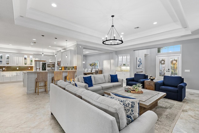 living room with crown molding, french doors, a tray ceiling, and a chandelier