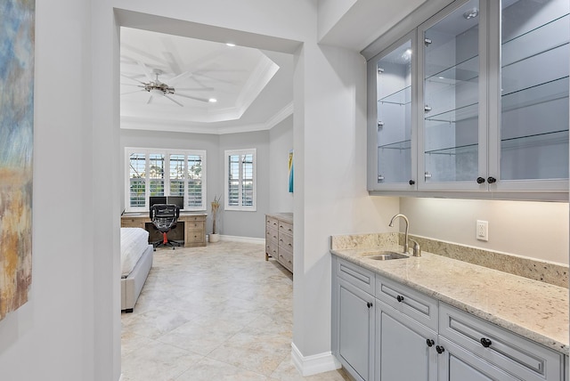 bar featuring ceiling fan, a raised ceiling, sink, crown molding, and light stone countertops