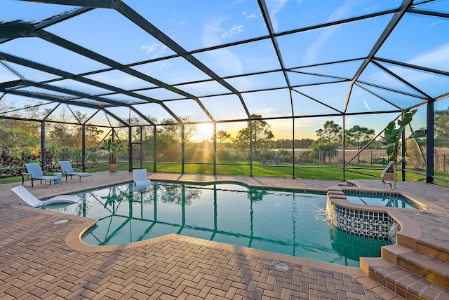 pool at dusk featuring a lanai, a patio area, and an in ground hot tub