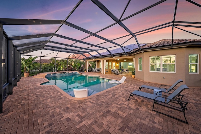 pool at dusk featuring a lanai, a patio area, and an in ground hot tub