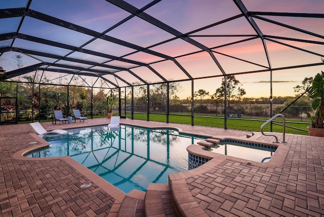 pool at dusk with glass enclosure, a patio area, an in ground hot tub, and a yard