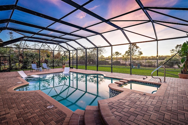 pool at dusk with a lanai, a lawn, a patio area, and an in ground hot tub