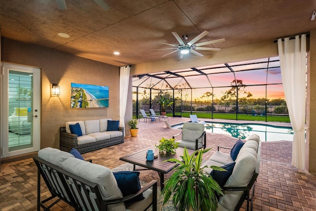 patio terrace at dusk featuring glass enclosure, ceiling fan, and an outdoor hangout area