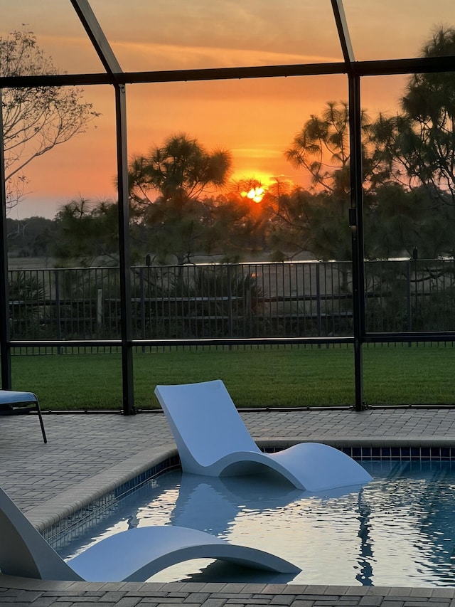 pool at dusk featuring a lanai, a patio area, and a yard