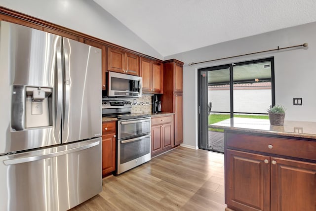 kitchen with lofted ceiling, stainless steel appliances, light hardwood / wood-style floors, decorative backsplash, and light stone counters