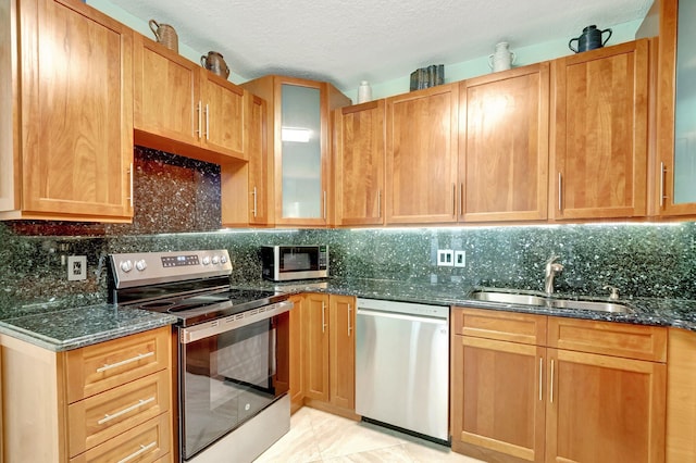 kitchen with dark stone counters, sink, decorative backsplash, light tile patterned floors, and appliances with stainless steel finishes