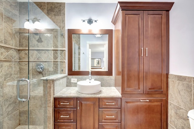 bathroom featuring vanity, toilet, a shower with door, and tile walls