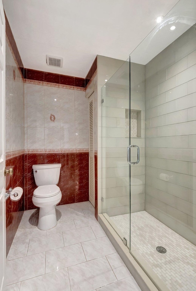 bathroom with tile patterned floors, toilet, a shower with door, and tile walls