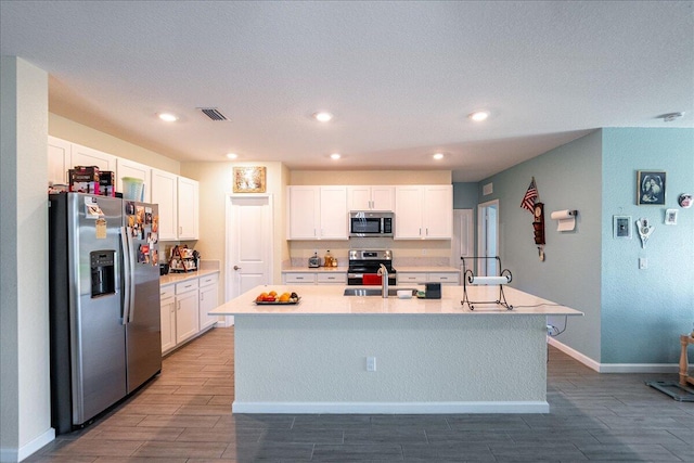 kitchen with stainless steel appliances, white cabinetry, a kitchen island with sink, and sink