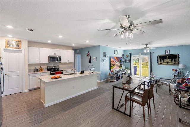 kitchen with sink, a textured ceiling, a center island with sink, white cabinets, and appliances with stainless steel finishes